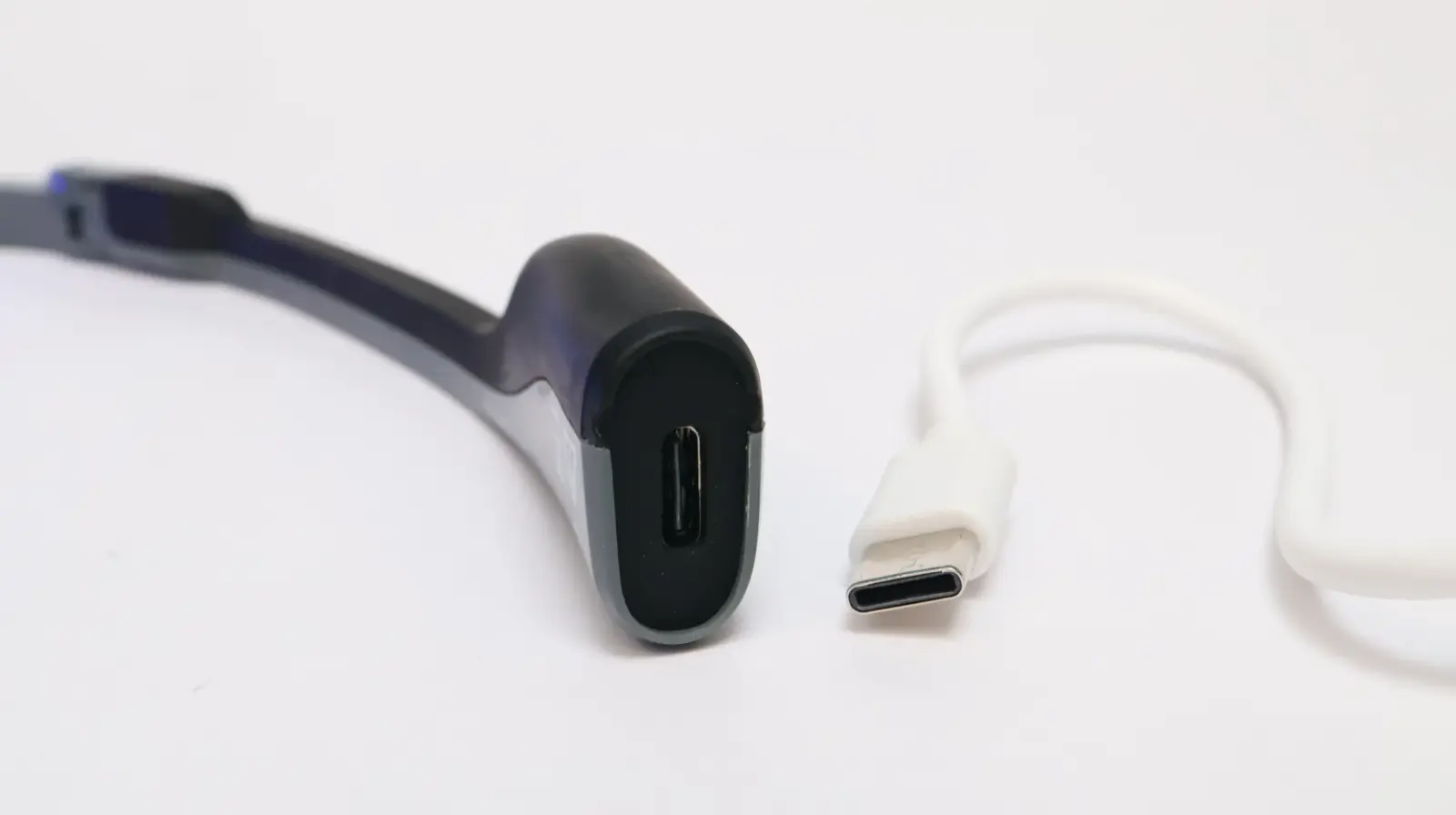 USB-C port on a smart glasses temple arm next to a white USB-C charging cable on white background