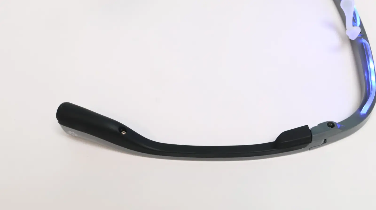 Black temple arm of sport sunglasses with blue mirrored lens and rubber tip, laid flat on white surface