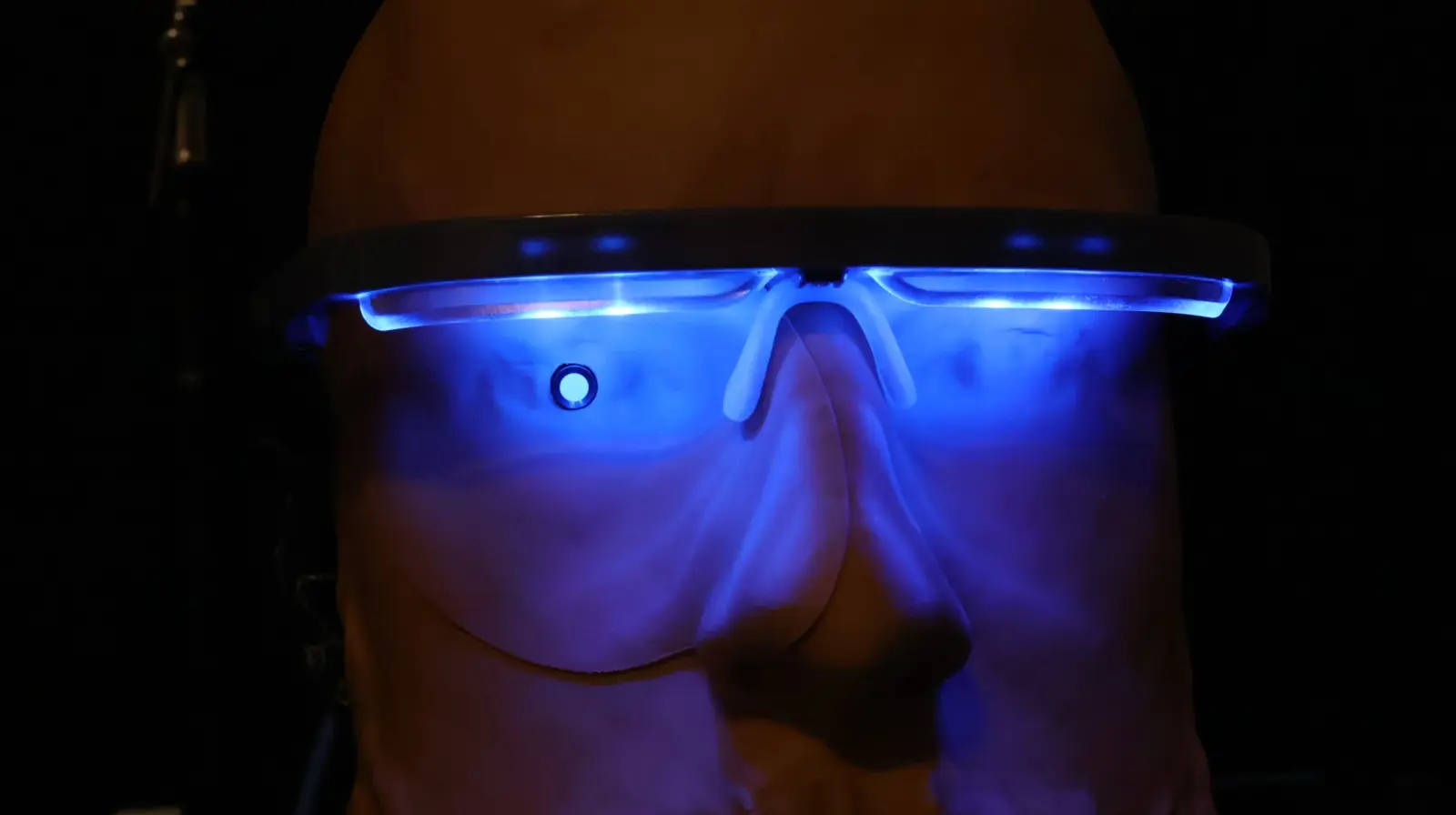 Bald person wearing futuristic blue LED-lit smart glasses glowing in the dark