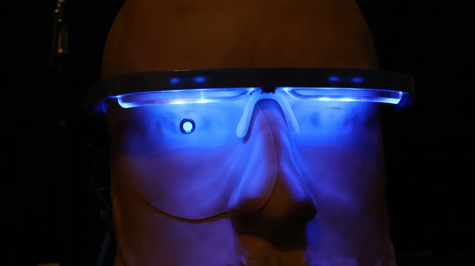 Bald person wearing futuristic blue LED-lit smart glasses glowing in the dark