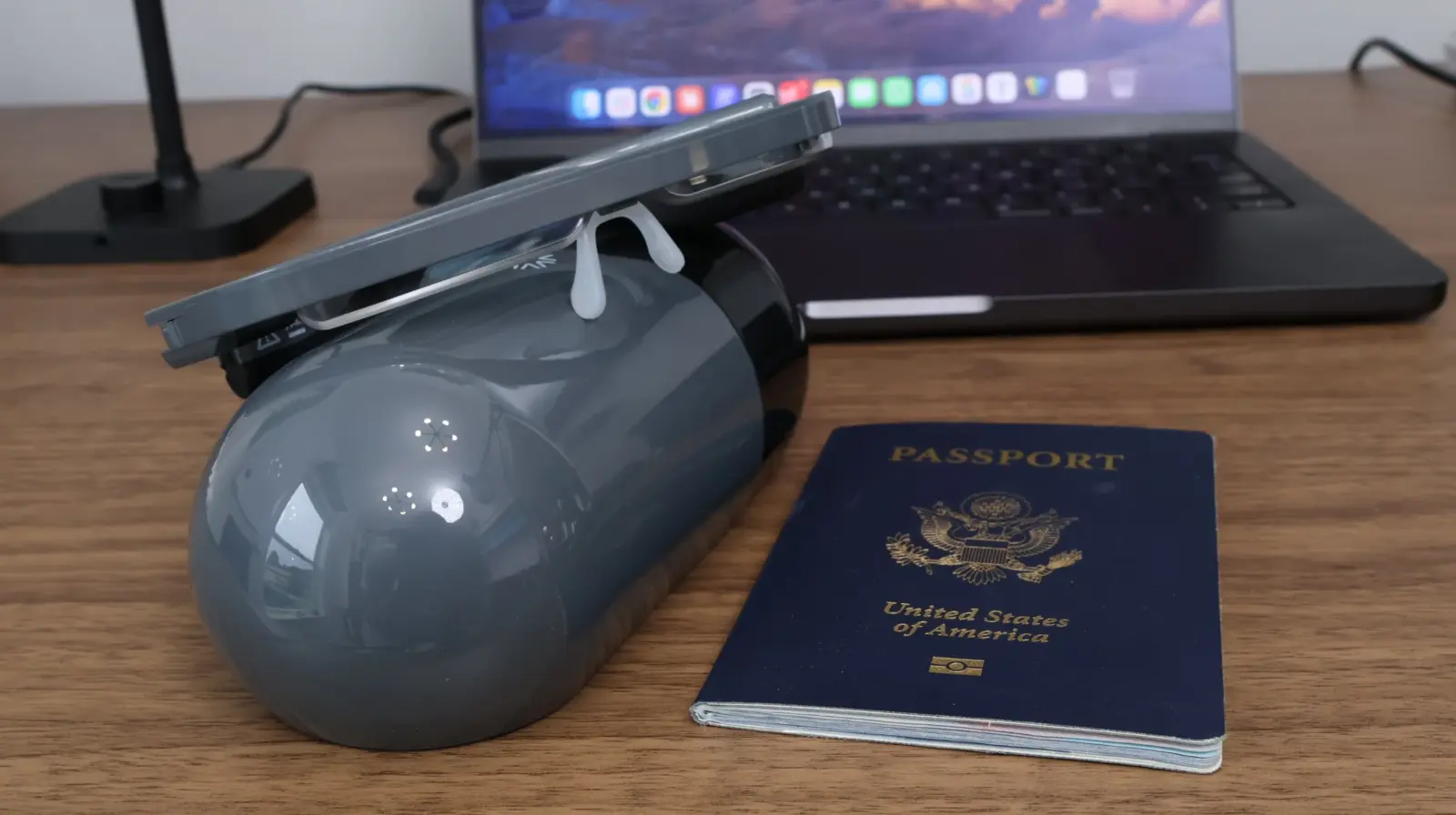 Gray portable vacuum cleaner beside a US passport and laptop on a wooden desk
