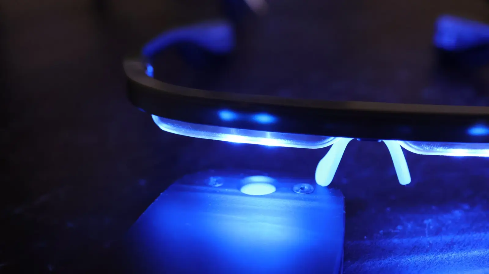 Blue UV LED light illuminating a circular optical lens assembly mounted on a dark mechanical fixture
