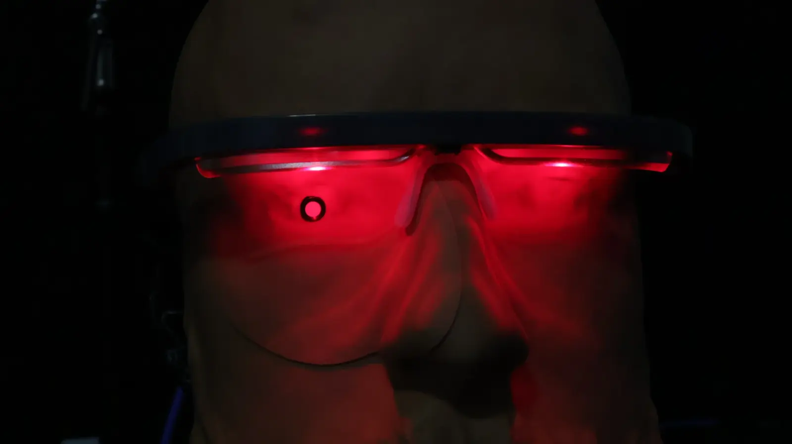 Person wearing illuminated red LED light therapy glasses in a dark room during a photobiomodulation session