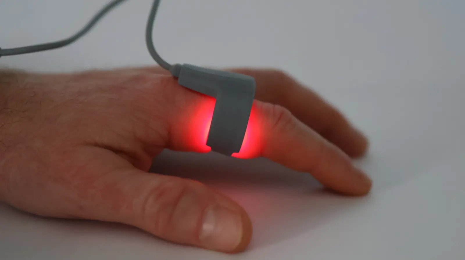 Pulse oximeter sensor clipped on finger glowing red, used for blood oxygen saturation and heart rate monitoring