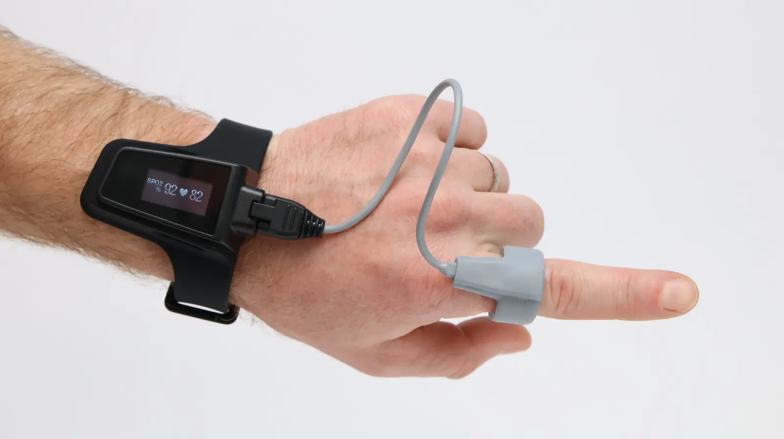 Wrist-worn pulse oximeter with finger sensor displaying SPO2 92% and heart rate 82 BPM on OLED screen
