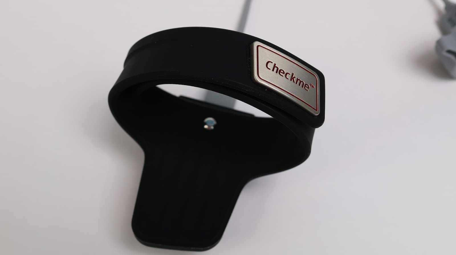 Checkme branded black silicone wrist pulse oximeter sensor with cable, displayed on white surface