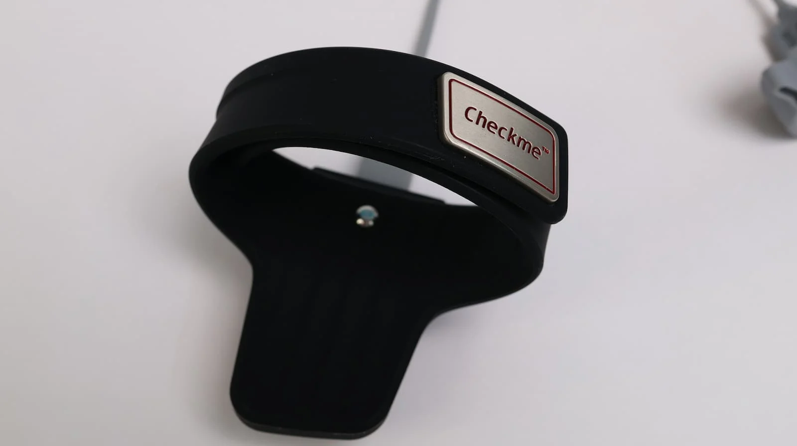 Checkme branded black silicone wrist pulse oximeter sensor with cable, displayed on white surface