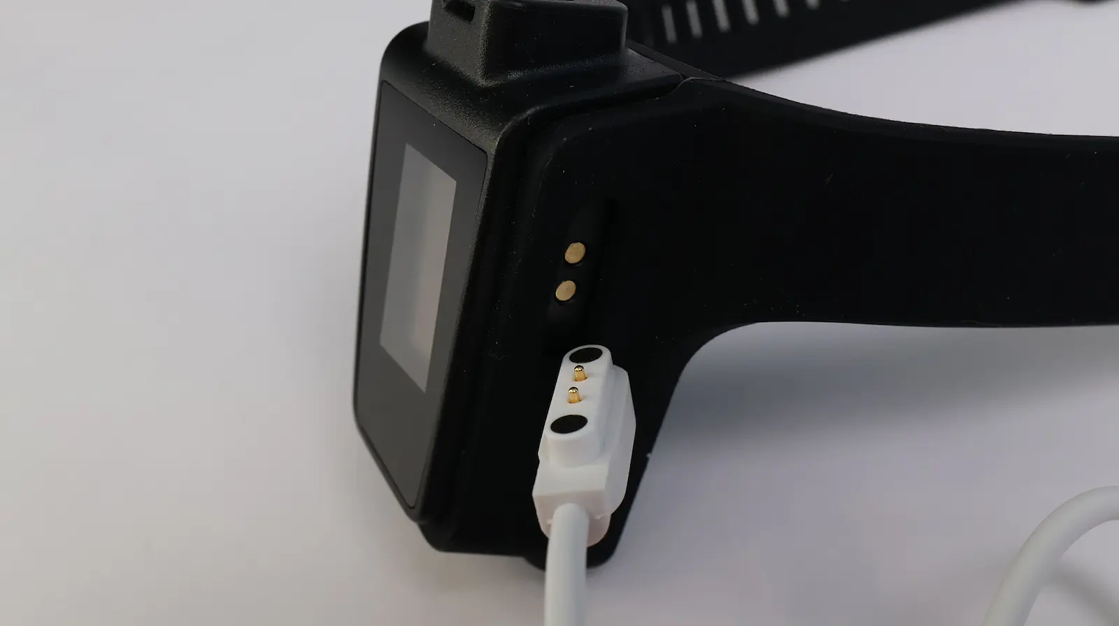 Black smartwatch being charged with a white magnetic pogo-pin charging cable on a white surface