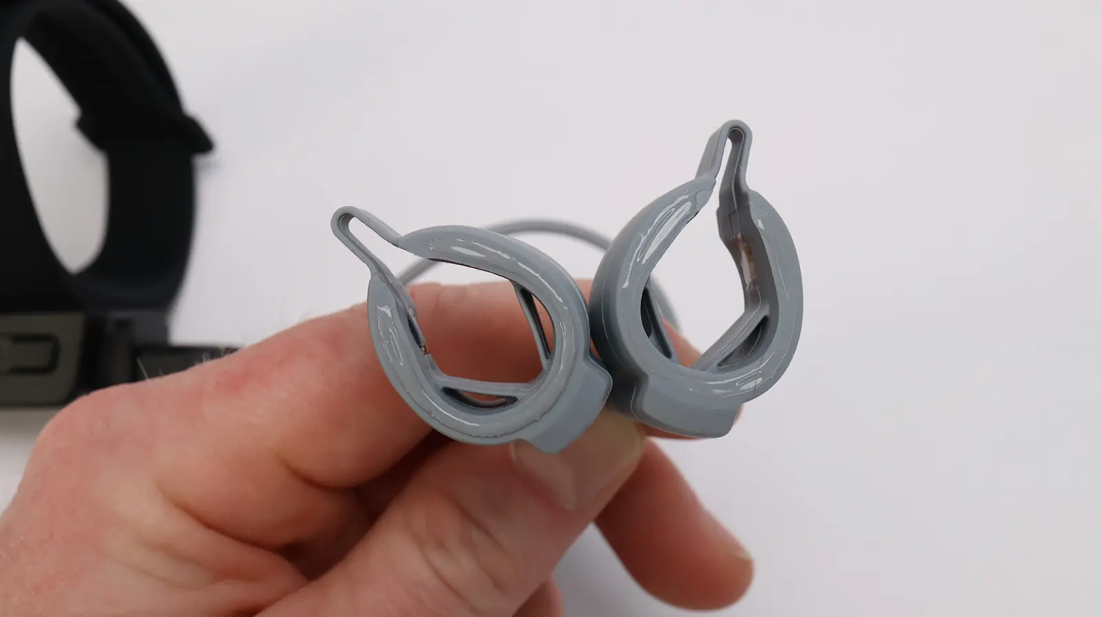 Hand holding a pair of gray open-ear bone conduction sport earphones with ear hook clips connected by a cable