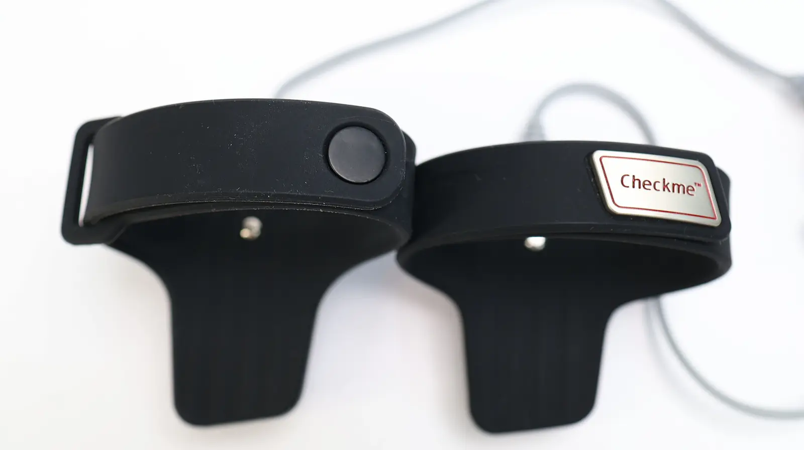 Two black Checkme wearable health monitoring wristbands side by side on white surface, one with button and one with branded l
