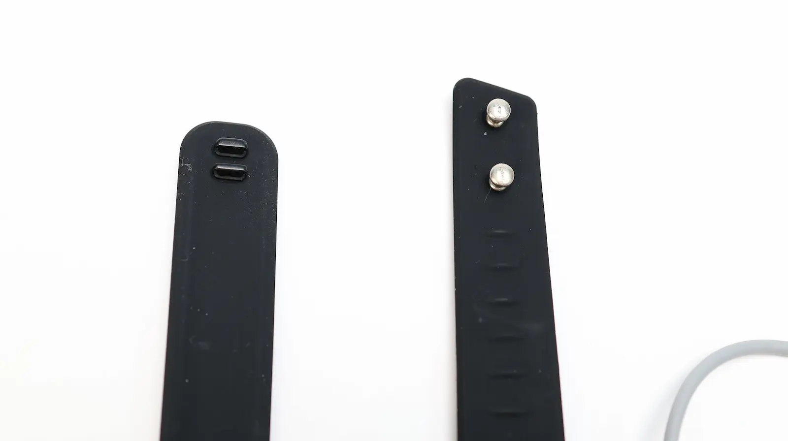 Two black silicone fitness tracker band ends side by side, one with charging contacts and one with metal clasp pins