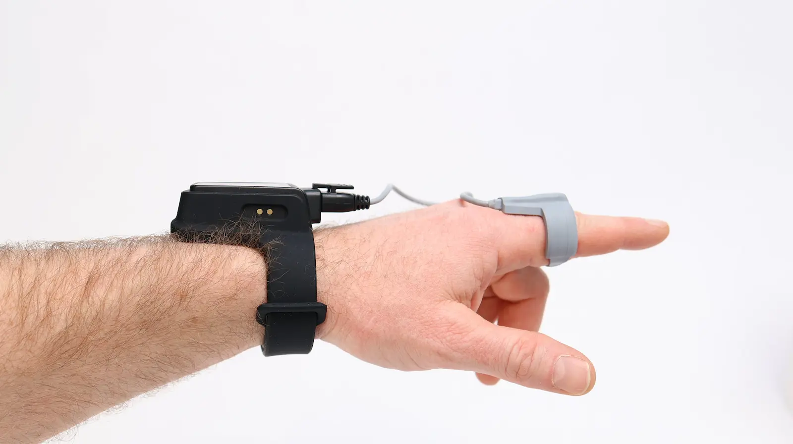 Wrist-worn health monitor connected via cable to a finger pulse oximeter sensor on a human hand