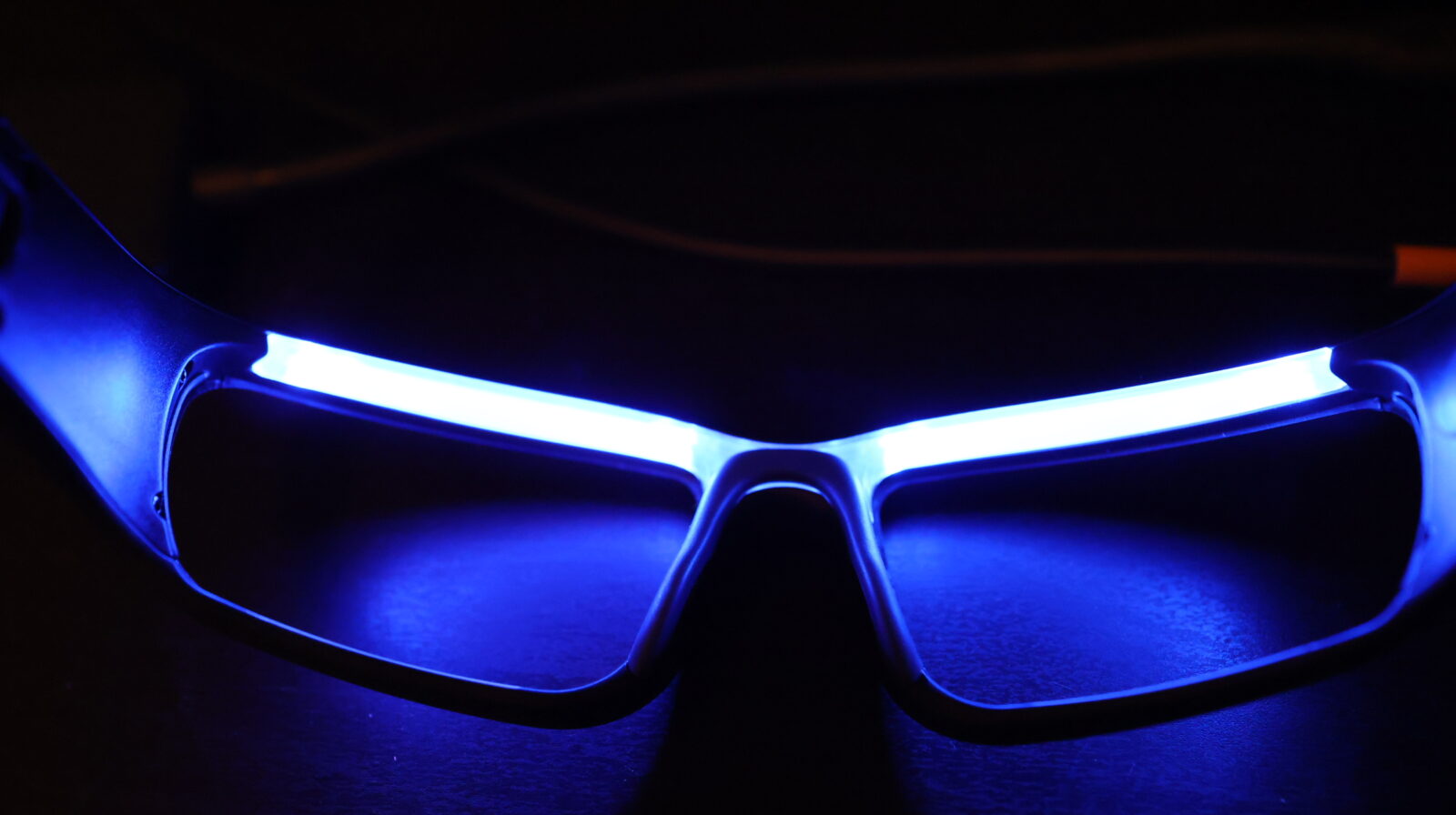 Futuristic LED-lit glasses glowing electric blue in the dark, resting on a surface with neon light strips