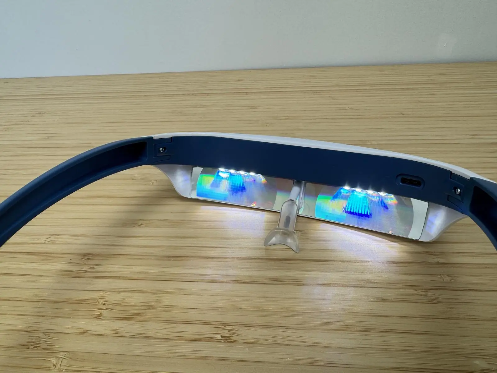 Luminette 2 light therapy glasses turned on, showing glowing LEDs and reflective lenses on a wooden table.