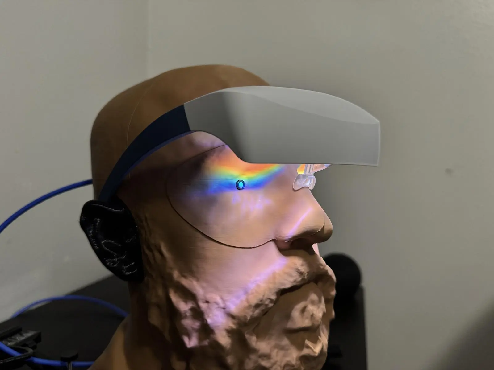 Luminette 2 on a bearded headform, with rainbow light spread across the face beside a small blue sensor.