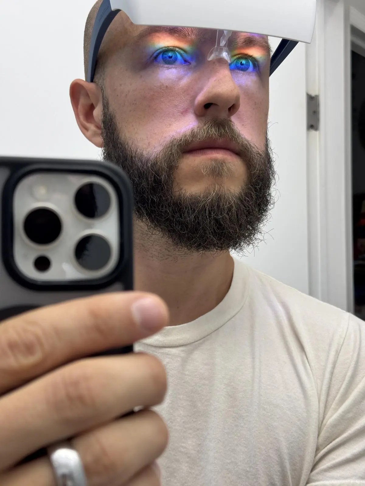 Bearded man taking a phone selfie while wearing a Luminette 2 light therapy device, with blue light visible on his eyes.