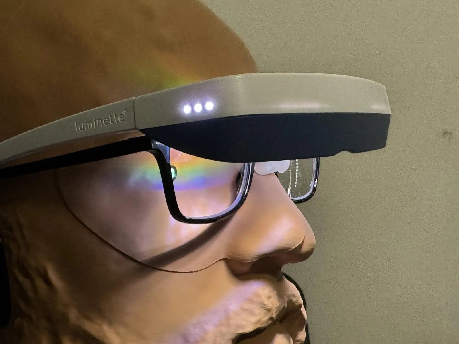 Luminette 3 light therapy glasses worn over clear-lensed black frames on a headform, with three small lights on the top band.