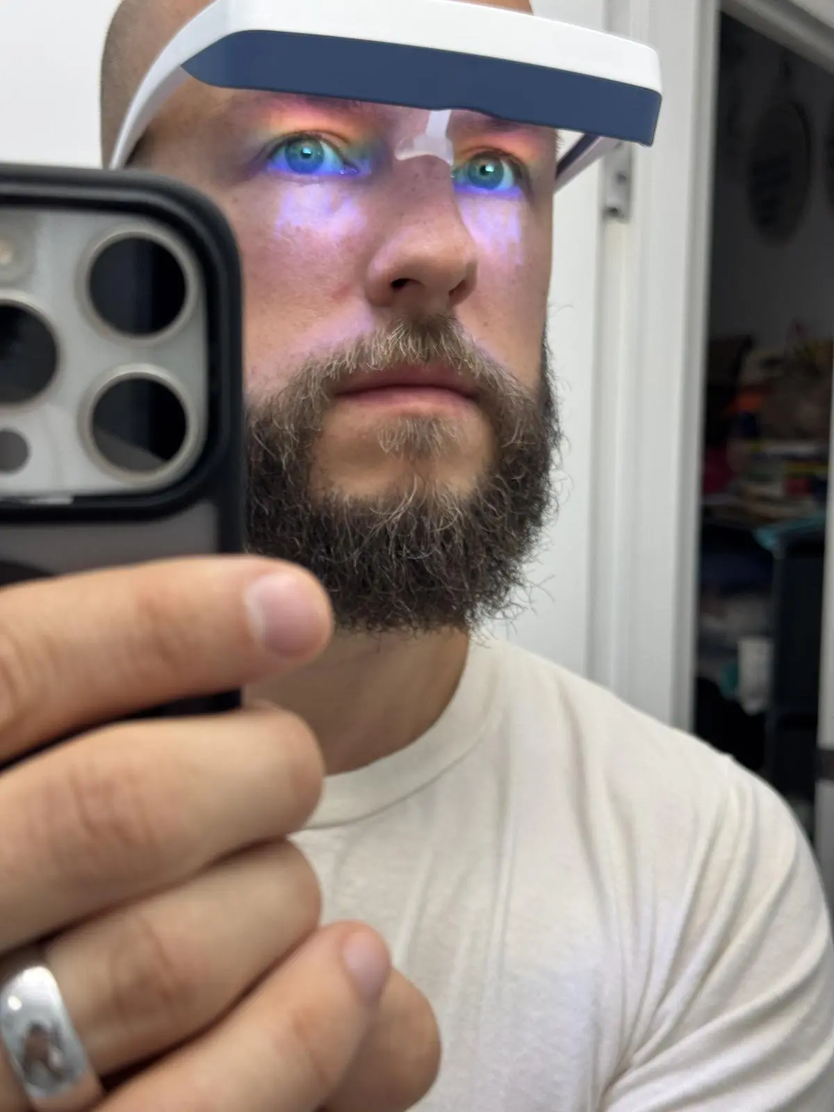 Bearded man taking a mirror selfie while wearing a Luminette 3 device, with blue light directed into his eyes.