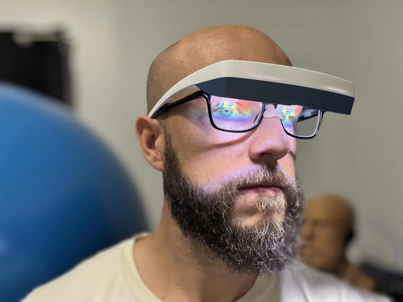 Bearded man wearing the Luminette 3 visor over black-framed glasses, seen in three-quarter view, with light reflecting off the lenses.