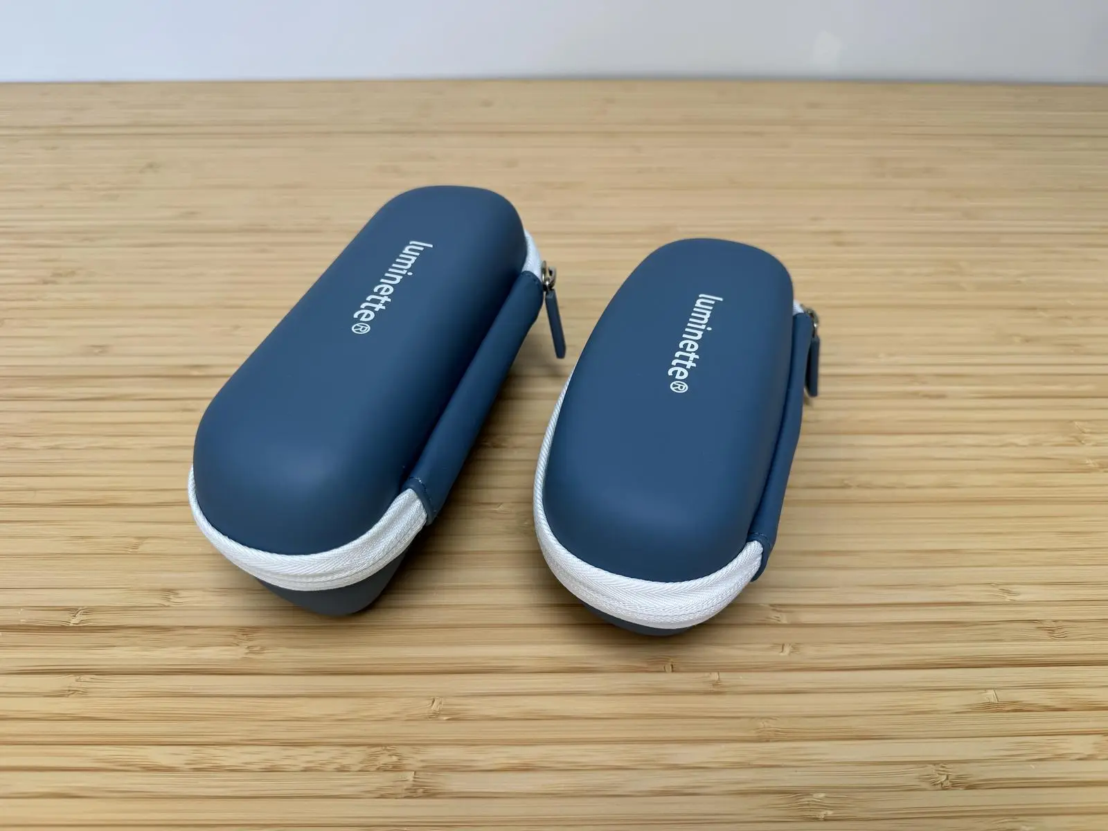 Two blue Luminette hard cases with white zipper trim, closed and placed side by side on a wooden surface.